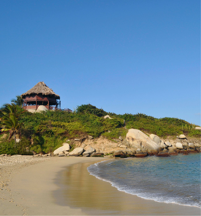 small beach front next to a hill covered in grass with a thatched hut at the top