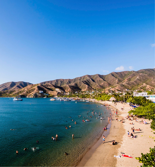 beachfront with people swimming, with mountains in the background and some boats