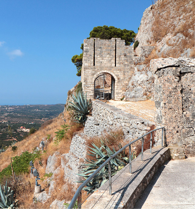 stone walls and walkways on the edge of a cliff surrounded by scarce desert style plants 