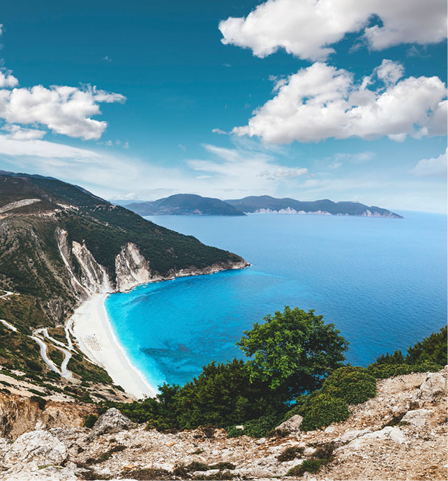 aerial view of a beach cove surrounded by mountains and cliff faces with vibrant blue water 