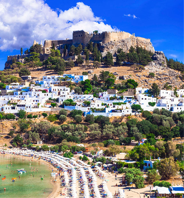 Beach next to a town of white buildings on a hill with a fortress at the top