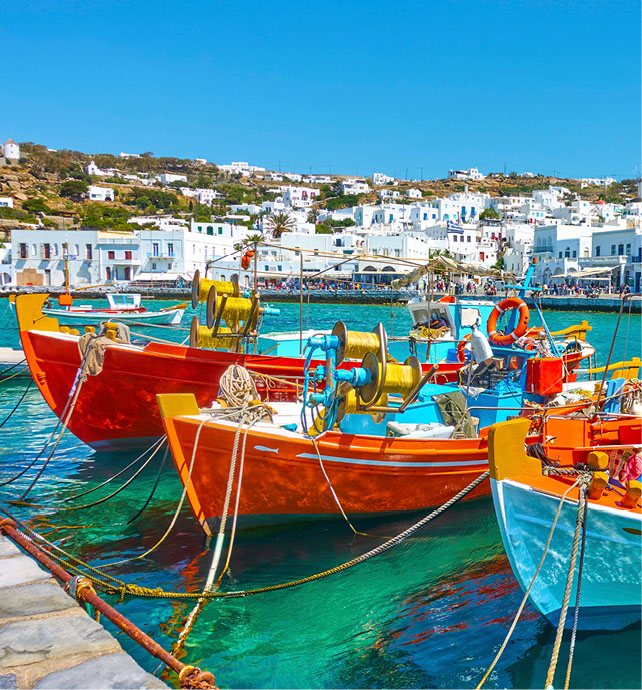 bright coloured painted boats in the turquise blue water with white buildings behind