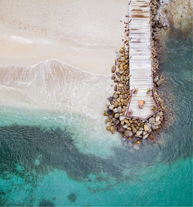 aerial view of a boardwalk on top of rocks next to the blue ocean and white sand