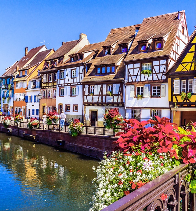 A row of white and brown thatched houses covered in bright coloured flowers next to a river