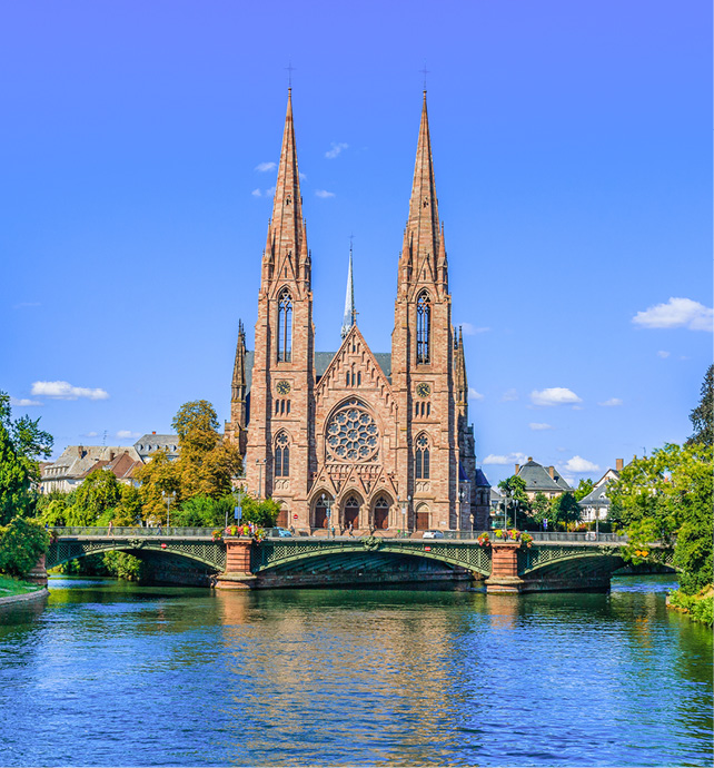 Cathedral with two spires behind a bridge and a river.