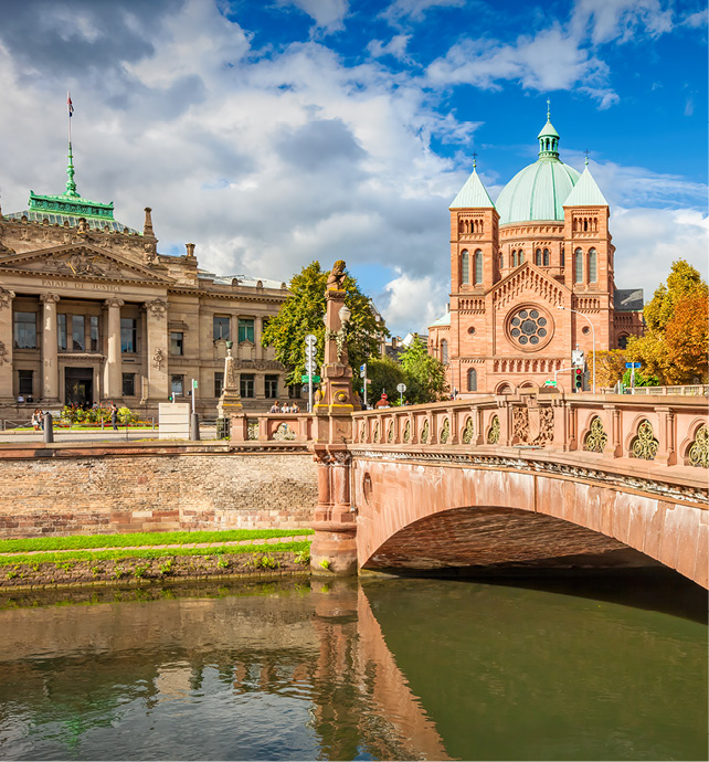 bridge and river in front of a orange brick church with a green domed roof