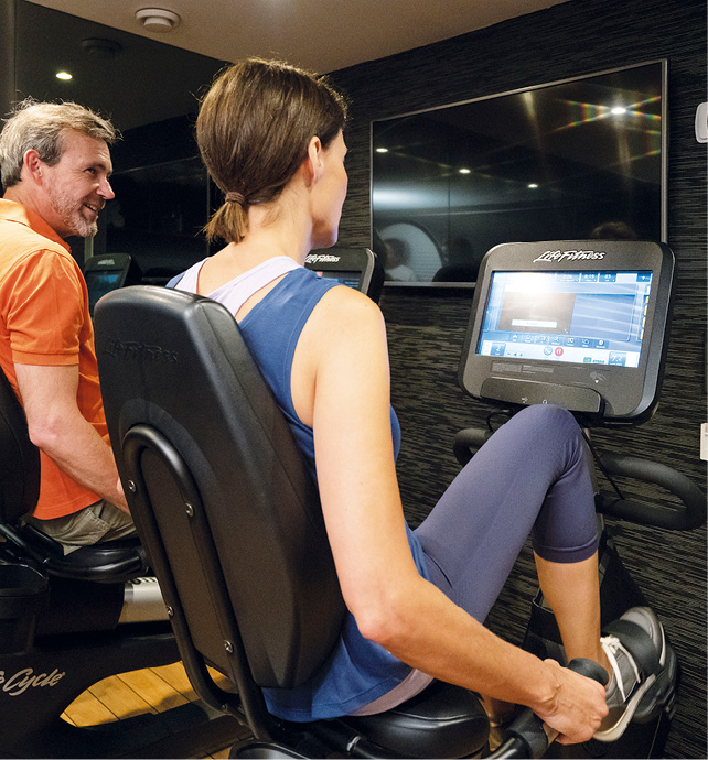 Two guests using innovative cycling machines with LED screen to exercise their leg muscles in the gym