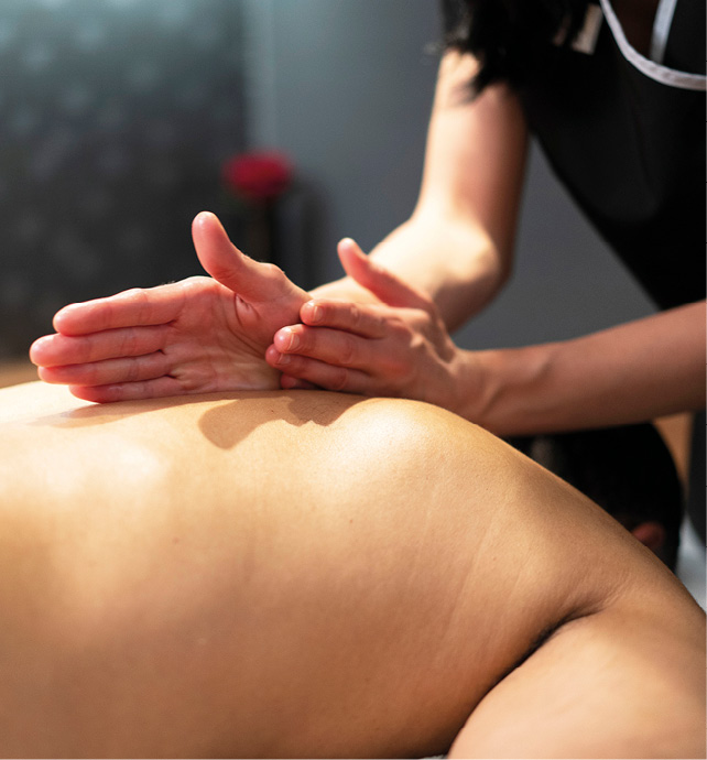 Close-up shot of a man receiving a back massage in a therapy room, with the masseuse’s hands and arms working through his muscles