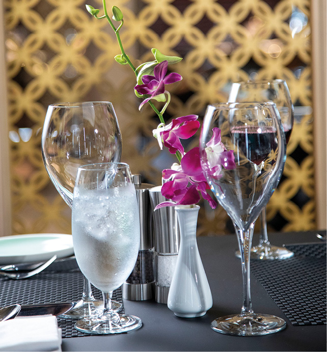 Highly polished wine glasses set on the table for an evening meal, with a flower and vase centrepiece