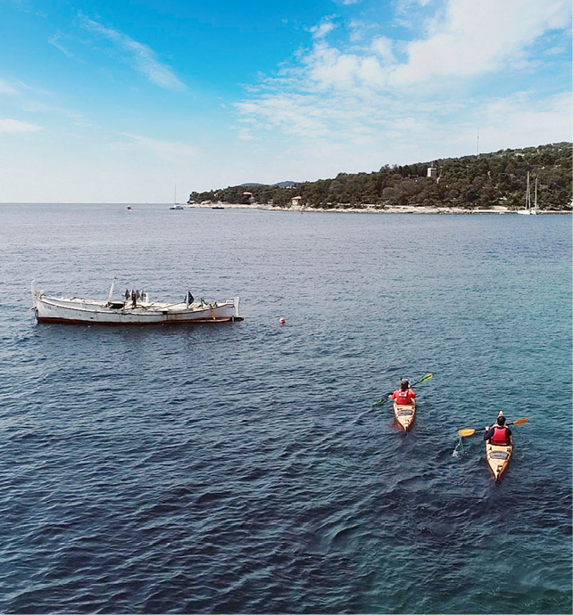 Two guests kayaking along the coast heading back to their luxury yacht cruise in the distance